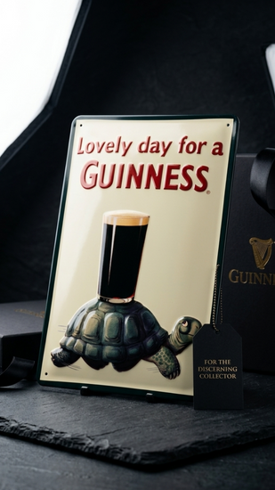 Guinness sign with turtle holding a glass of Guinness on a dark surface