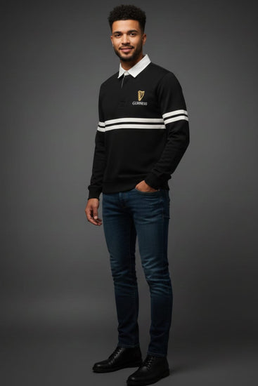 Man wearing a black sweater with white stripes and a logo, standing against a gray background