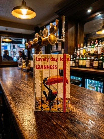 Wooden sign with a toucan illustration and 'Lovely day for a GUINNESS' text on a bar counter.